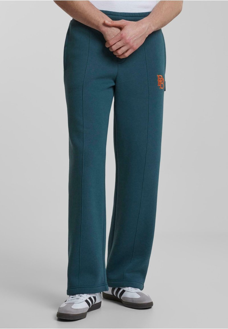 Pantalones de chándal color teal con cintura elástica, que presentan bolsillos laterales y un logo bordado en naranja. Fabricados con una tela suave y texturizada.