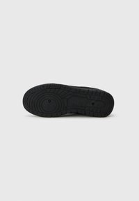 Black rubber sole with a textured pattern, featuring circular grooves and ridges for grip. Smooth finish with a rounded toe shape.