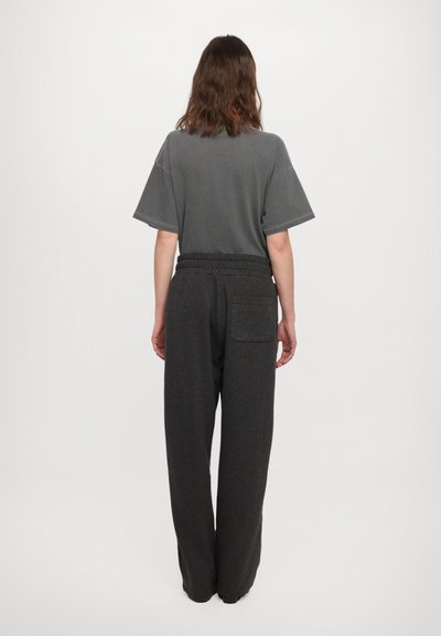 Camiseta gris de manga corta y corte holgado, combinada con pantalones de chándal gris oscuro que tienen una cintura elástica y un bolsillo trasero.