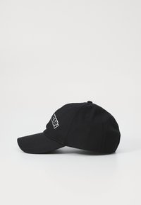Čierna bavlnená baseballová čiapka s vyšitou nášivkou vpredu. Zakrivený šilt a nastaviteľný popruh vzadu. Minimalistický dizajn.