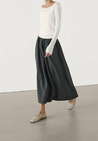 Hvid langærmet top sammen med en mørkegrå, let skørt og lysebeige flade sko. Outfittet har et simpelt, minimalistisk design.