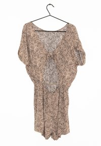 Vestido beige de corte holgado, con un estampado de animal, mangas cortas, escote en V profundo y una espalda descubierta. Cuelga de un gancho negro.