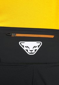 Haut de sport noir avec un design texturé, doté d'une poche zippée orange et d'un logo blanc en forme de triangle avec un visage stylisé.
