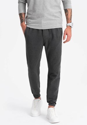Gray jogger pants made of soft fabric, featuring a tapered design with elastic cuffs and an elastic waistband, paired with white sneakers.