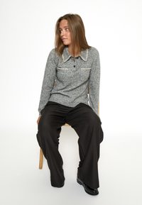 Maglione grigio a maniche lunghe con colletto, dotato di due tasche frontali e cuciture a contrasto, abbinato a pantaloni neri a gamba larga e scarpe nere.