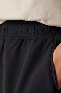 Pantalones cortos deportivos negros con una cinturilla texturizada con "SEVEN DEGREES" grabado. La tela parece suave con un ligero brillo.