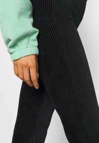 Mintgrøn sweatshirts med sammenfoldede manchetter, parret med sorte ribbede leggings. Fokus på struktureret stof og tætsiddende design. Hånd hviler nær leggings.