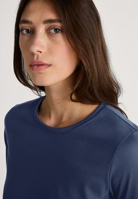 Navy blue, long-sleeve top with a crew neck, made from a smooth fabric. Features a close-fitting silhouette and subtle shoulder details.
