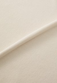 Tissu tissé beige avec une surface texturée et un léger nervurage, plié en diagonale, mettant en valeur son matériau robuste et sa couleur claire.