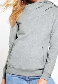Sweat-shirt gris à col bénitier, manches longues et deux poches frontales. Le matériau semble doux avec une texture lisse. Coupe décontractée avec un ourlet côtelé.