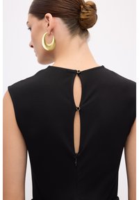 Robe noire avec un détail de dos en trou de serrure, dotée d'une petite fermeture éclair et d'accents en métal doré. Tissu lisse avec des manches courtes.