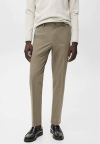 Beige op maat gemaakte broeken met een slim fit, voorzien van een platte voorkant, knoopsluiting en zijzakken, gecombineerd met zwarte loafers.
