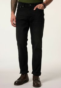 Jeans de mezclilla negra con corte recto, diseño de cinco bolsillos y un ligero desgaste, combinados con botas de cuero marrón.