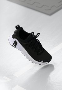 Zwarte sportieve schoen met een bovenwerk van mesh, witte zool en opvallende groeven. Beschikt over veters, een lus aan de achterkant en logo-accenten aan de zijkant.