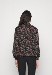 Blusa floral com fundo preto, apresentando padrões florais em rosa e verde, mangas longas e decote com pregas. Textura semelhante ao cetim.