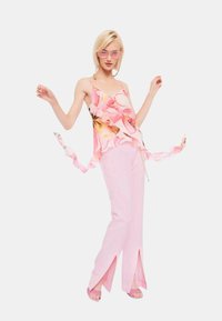 Top senza maniche floreale rosa con volant, abbinato a pantaloni palazzo rosa chiaro con fessure laterali. I tacchi sono anch'essi rosa con un design testurizzato.