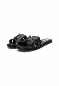 Chanclas de cuero negro con dos hebillas anchas y recortes, suelas planas y un acento metálico. Textura suave y diseño minimalista.