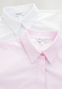 Deux chemises à col disposées à plat ; l'une blanche et l'autre rose pâle avec de fines rayures verticales. Les deux présentent une texture lisse et une étiquette visible à l'encolure.