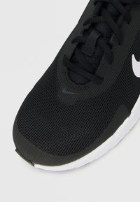 Czarny but do biegania marki Nike z siateczkową cholewką, czarnymi sznurówkami i białą podeszwą, pokazujący zbliżenie na palce i środkową część z logo.