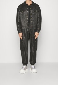 Svart metallisk jeansjacka och matchande cargobyxor med fickor. Har guldknappar, dragsko i midjan och vita oversized sneakers.