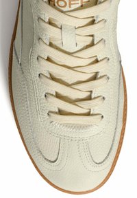 Zapatilla de cuero color blanco roto con superficie texturizada, cordones color crema atados en un patrón entrelazado y borde de suela de goma marrón claro.