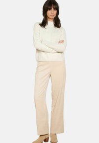 Beige Cordhosen mit lockerer Passform, kombiniert mit einem strukturierten, cremefarbenen Strickpullover mit hohem Kragen.