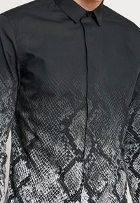 Black shirt with a button-up collar featuring a gradient snake skin pattern in gray and white on the lower half. Smooth fabric texture.
