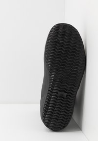 Svart snörskosula med ett texturerat fiskbensmönster, gjord av gummi. Sidan har subtila gropar som förbättrar grepp och dragkraft.