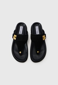 Sandali neri con suola piatta. Presentano una cinghia in suede, una fibbia dorata e un design a post per le dita. Sottopiede testurizzato con marchio.