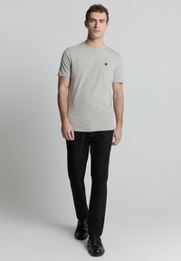 Kortarmig, lichtgrijze gestreepte t-shirt met klein rond logo, gecombineerd met zwarte broek en zwarte schoenen. Eenvoudig, slim fit ontwerp.