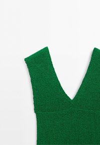 Close-up of a green knitted sleeveless top with a deep V-neck on a white background.