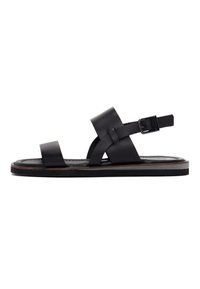 Black leather sandal with wide straps, a buckle closure, and a flat sole featuring a brown accent around the edge. Simple and minimal design.