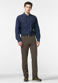 Mørkeblå denimskjorte med knopkrave og to brystlommer, parret med brune bukser og grønne sportsko. Glat tekstur.