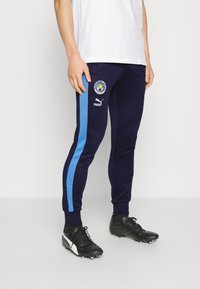 Navy Jogginghosen mit blauen Seitenstreifen, Puma-Logo und Manchester City-Wappen. Aus weichem Material, taillierter Schnitt mit gerippten Bündchen.