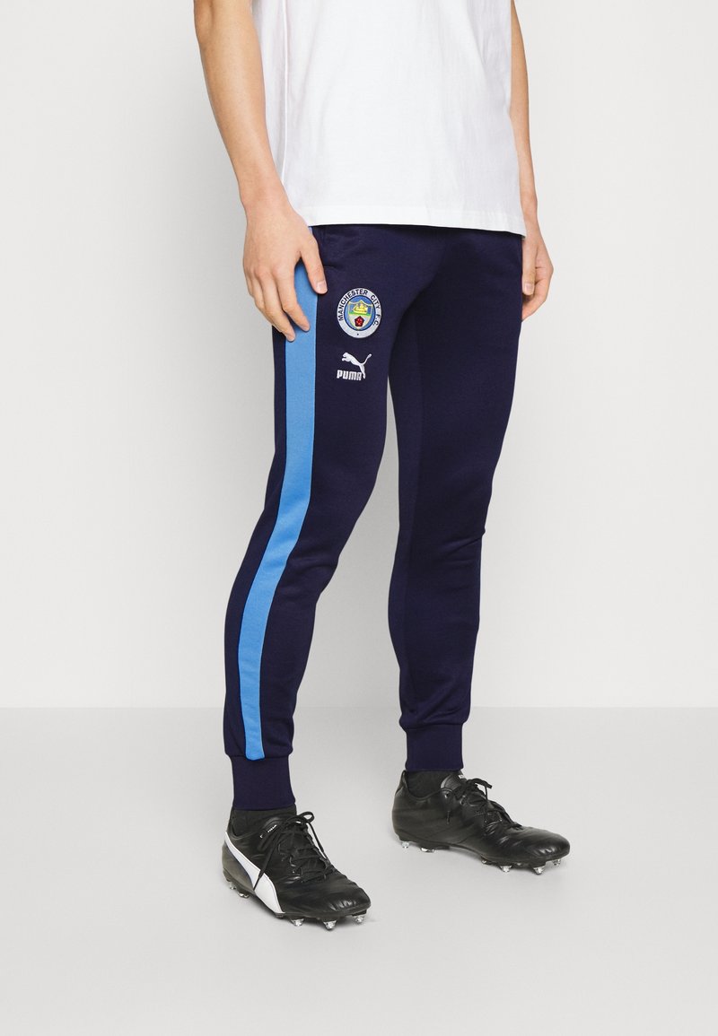 Navy Jogginghosen mit blauen Seitenstreifen, Puma-Logo und Manchester City-Wappen. Aus weichem Material, taillierter Schnitt mit gerippten Bündchen.