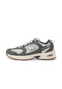 Šedé a bílé tenisky New Balance 530 s síťovanými panely, bílými tkaničkami, polstrovanou podrážkou a hnědou podrážkou, zobrazené v bočním profilu.