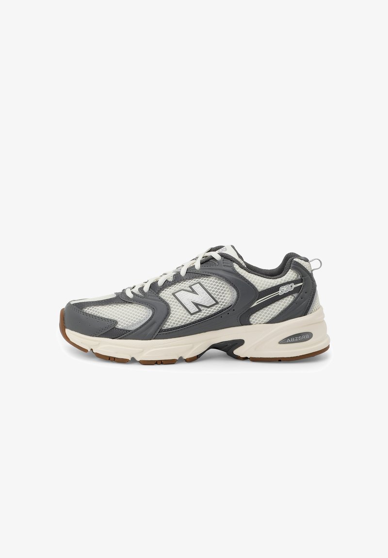 Šedé a bílé tenisky New Balance 530 s síťovanými panely, bílými tkaničkami, polstrovanou podrážkou a hnědou podrážkou, zobrazené v bočním profilu.