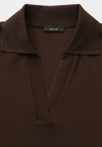 Braunes Poloshirt mit geripptem Kragen und V-Ausschnitt, gefertigt aus strukturiertem Stoff. Das Etikett trägt die Aufschrift "OPUS."