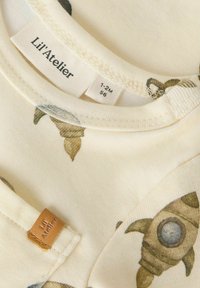 Koszulka bawełniana w kolorze kremowym z wzorem rakiet, z naszytą metką na szyi oraz małą skórzaną etykietą z wytłoczonym napisem "Lil'Atelier".