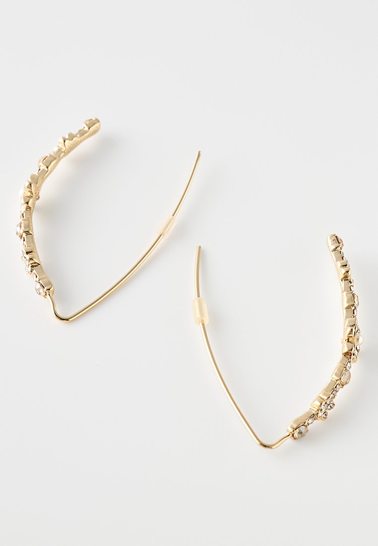 Goldene Creolen mit einem strukturierten Design, verziert mit klaren Strasssteinen, geschwungener Form und einer glatten, glänzenden Oberfläche.