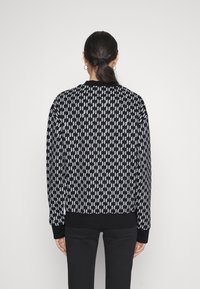 Schwarzer und weißer gemusterter Pullover mit langen Ärmeln, gerippten Bündchen und Rundhalsausschnitt. Ein geometrisches Design bedeckt den Stoff.