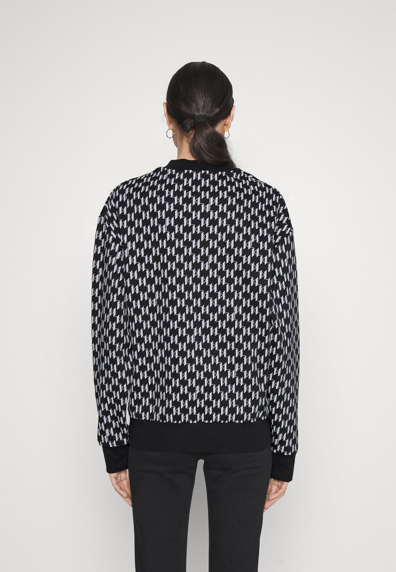 Schwarzer und weißer gemusterter Pullover mit langen Ärmeln, gerippten Bündchen und Rundhalsausschnitt. Ein geometrisches Design bedeckt den Stoff.