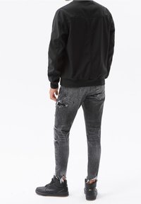 Black bomber jacket, gray distressed jeans with frayed hems, and black high-top sneakers. Focus on sleek design and textured materials.