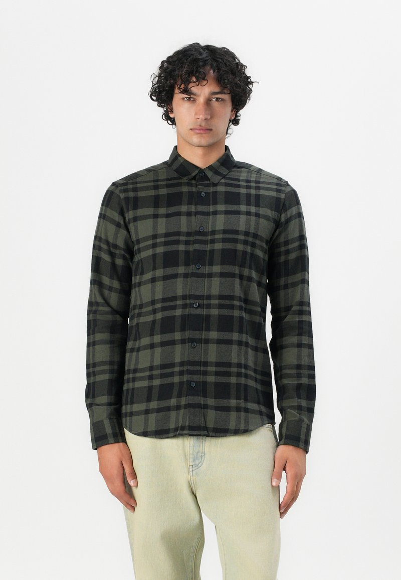 Camisa de cuadros en negro y verde oliva, de mangas largas, con frente abotonado, hecha de una tela suave con un cuello clásico y una textura sutil.