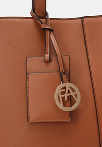 Borsa tote in finta pelle di colore tortora con una piccola tasca e un charm a forma di cerchio dorato. Presenta una finitura scura e dettagli con motivo intrecciato nella maniglia.