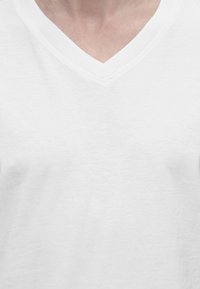 Gros plan sur une personne portant un t-shirt blanc uni à col en V, montrant le cou et la partie supérieure de la poitrine.