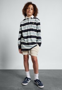 Gestreiftes langärmliges Poloshirt in Marineblau, Hellblau und Weiß, kombiniert mit beigen Shorts. Mit Logo auf der Brust und lässigen Sneakern.