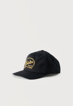 Sort baseballkasket med gul broderet "Brixton Quality MFG. Company" logo på fronten, vist mod en ensartet lys baggrund.