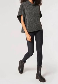 Poncho gris texturé avec col bénitier, associé à un jean skinny foncé et des bottines noires épaisses. La tenue est décontractée et moderne.