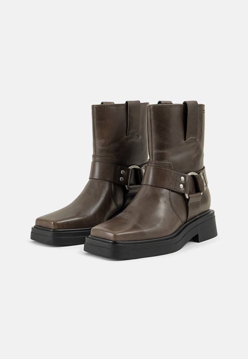 Braune Lederstiefeletten mit quadratischer Zehenform, versehen mit einem metallischen Akzentriemen, glatter Textur und einer auffälligen schwarzen Gummisohle.